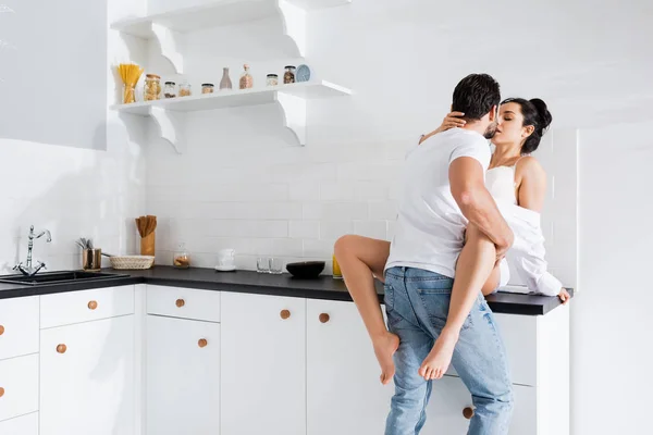 Menina sedutora no sutiã e camisa beijando namorado na bancada da cozinha — Fotografia de Stock