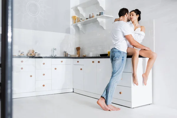 Selective focus of man kissing beautiful girlfriend in shirt and bra on kitchen worktop — Stock Photo