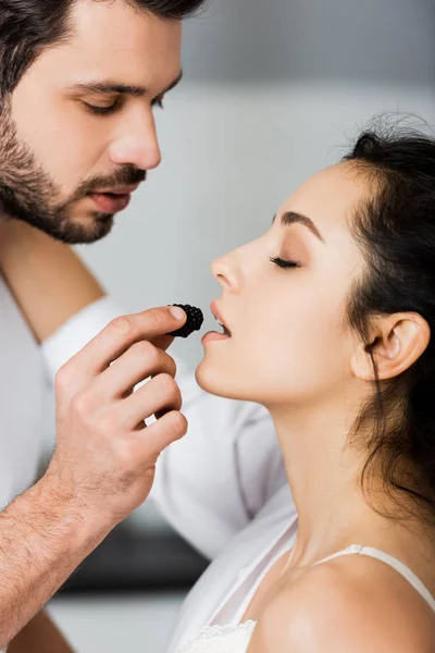 Vue latérale d'un bel homme nourrissant sa copine sexy avec une mûre — Photo de stock