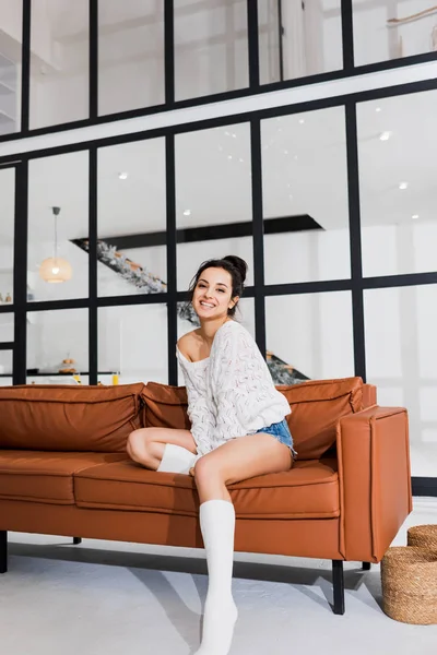 Красива жінка посміхається на камеру, сидячи на дивані у вітальні — стокове фото