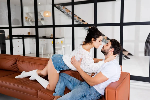 Side view of sexy girl hugging handsome boyfriend on couch in living room — Stock Photo