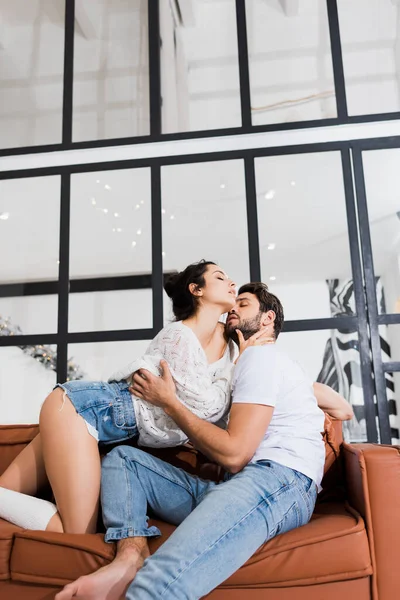 Low angle view of handsome man kissing sensual girlfriend on sofa — Stock Photo