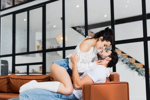 Vista laterale della donna attraente baciare fidanzato sul divano — Foto stock
