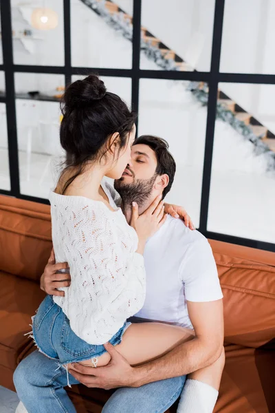 Handsome man kissing and holding by buttocks sexy girl on couch — Stock Photo