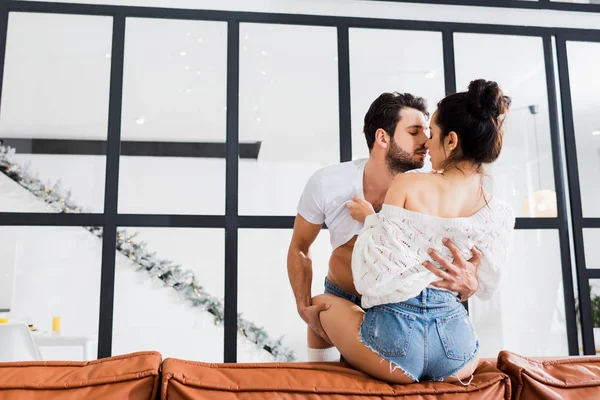 Verführerische Frau zieht Freund auf Couch im Wohnzimmer aus — Stockfoto