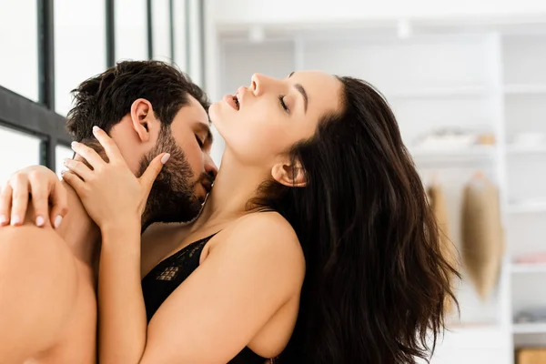 Side view of handsome man kissing in kick beautiful woman in bra at home — Stock Photo