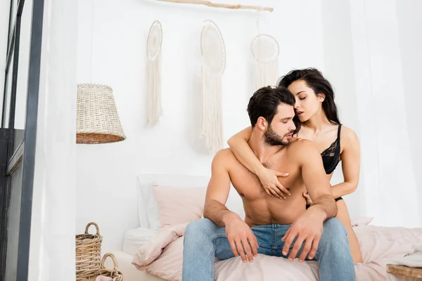 Passionate woman in underwear touching chest of shirtless man on bed — Stock Photo