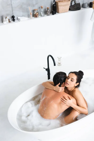 Vue grand angle de la femme séduisante embrassant petit ami musclé dans le bain avec mousse — Photo de stock