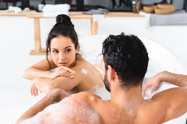Selective focus of sensual woman looking at boyfriend while taking bath with foam together — Stock Photo
