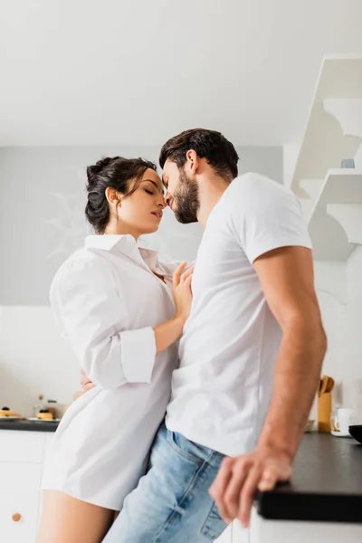 Vista laterale della ragazza sensuale in camicia baciare bel ragazzo vicino al piano di lavoro della cucina — Foto stock