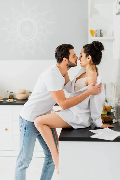 Perfil de homem bonito decolando camisa de namorada sexy na bancada da cozinha — Fotografia de Stock
