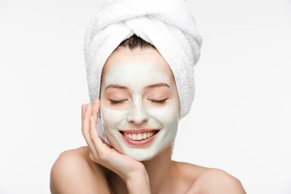 Happy girl with facial nourishing mask and towel on head touching face with closed eyes isolated on white — Stock Photo