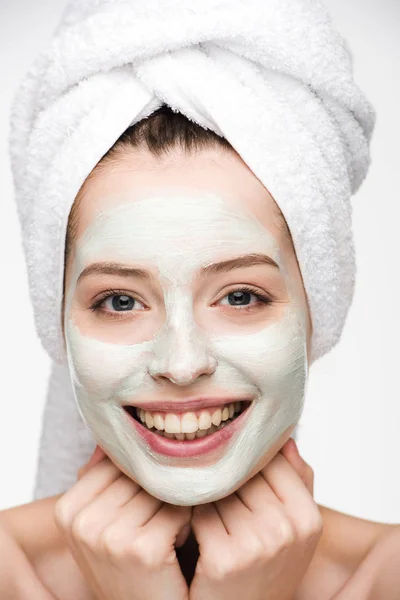 Счастливая девушка с питательной маской для лица и полотенцем на голове, глядя на камеру, изолированную на белом — стоковое фото