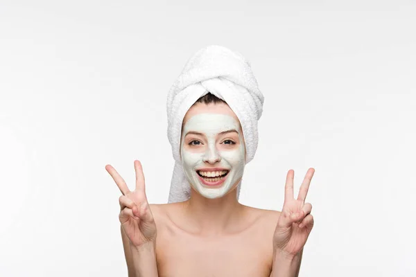 Chica sonriente con mascarilla facial nutritiva y toalla en la cabeza mostrando gestos de victoria aislados en blanco - foto de stock