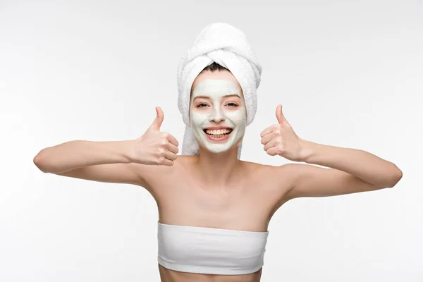 Happy girl with nourishing facial mask and towel on head showing thumbs up isolated on white — Stock Photo