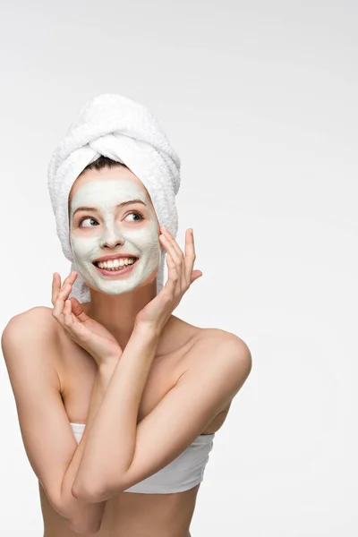 Sorridente ragazza con maschera nutriente viso e asciugamano sulla testa toccare il viso isolato su bianco — Foto stock