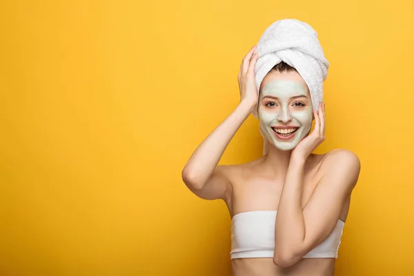 Menina feliz com nutritivo máscara facial tocando toalha na cabeça no fundo amarelo — Fotografia de Stock