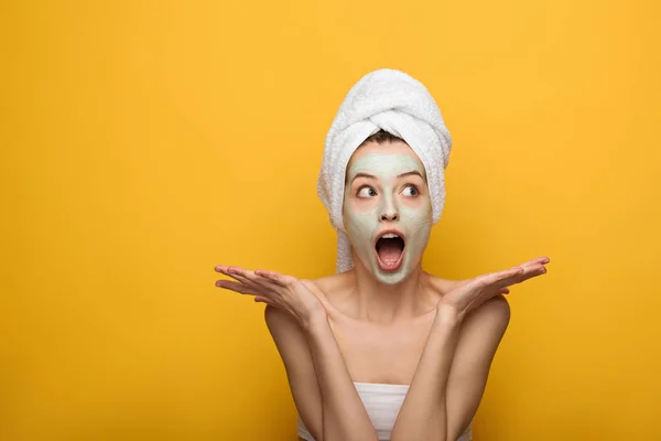 Schockiertes Mädchen mit pflegender Gesichtsmaske mit Achselzucken-Geste auf gelbem Hintergrund — Stockfoto