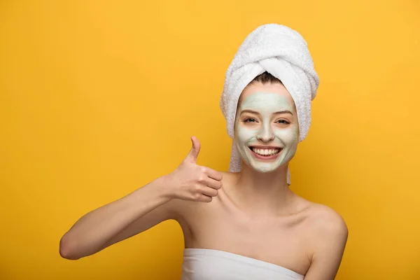 Happy girl with nourishing facial mask showing thumb up and smiling at camera on yellow background — Stock Photo