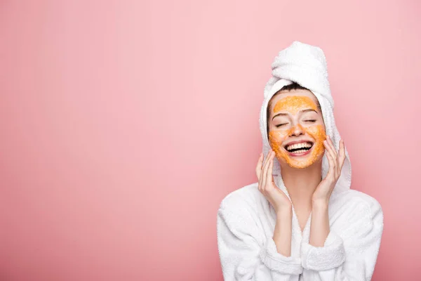 Glückliches Mädchen mit Zitrusgesichtsmaske berührt Gesicht mit geschlossenen Augen isoliert auf rosa — Stockfoto