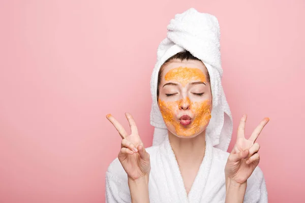 Young woman with citrus facial mask showing victory gestures isolated on pink — Stock Photo