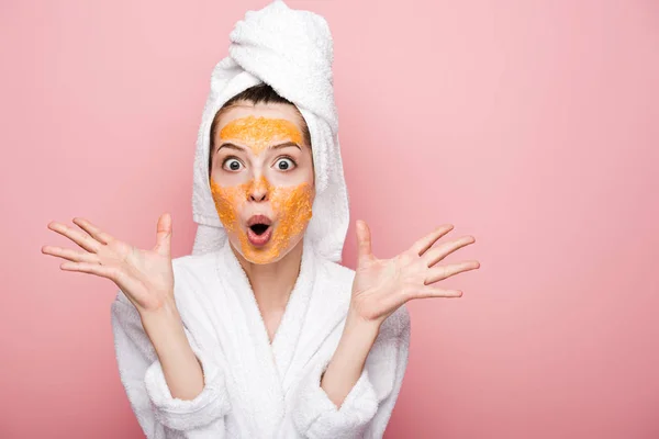 Impactado chica con cítricos máscara facial de pie con los brazos abiertos sobre fondo rosa - foto de stock