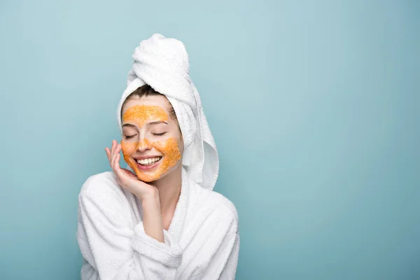 Menina feliz com máscara facial cítrica tocando rosto com olhos fechados isolados em azul — Fotografia de Stock