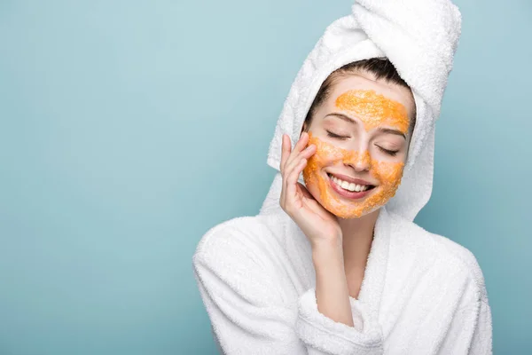 Smiling girl with citrus facial mask touching face with closed eyes isolated on blue — Stock Photo