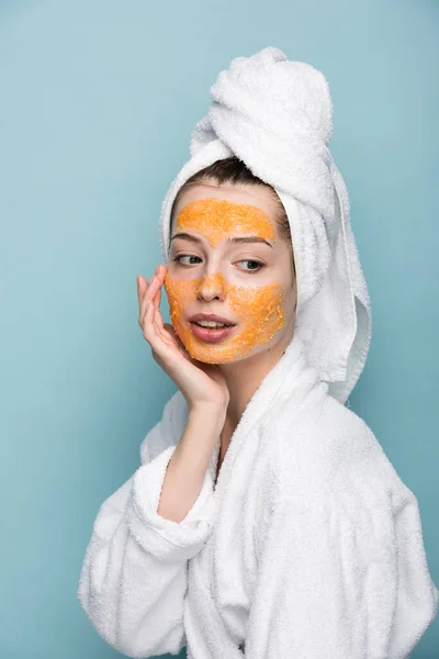 Ragazza pensosa con agrumi maschera facciale toccare viso isolato su blu — Foto stock