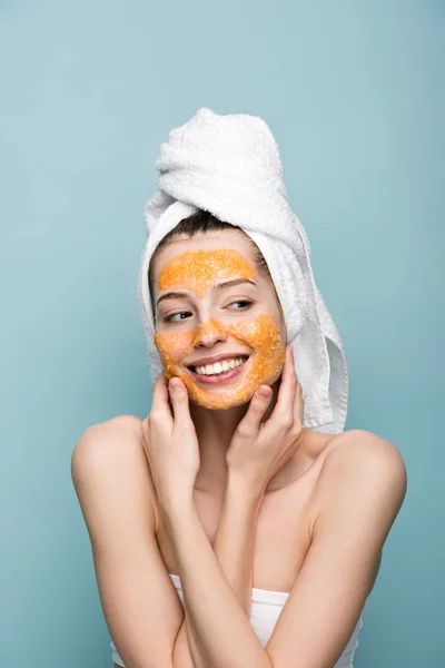 Cheerful girl with citrus facial mask looking away and touching face isolated on blue — Stock Photo