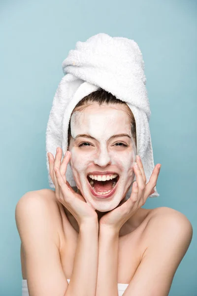 Excited girl with moisturizing facial mask laughing at camera isolated on blue — Stock Photo