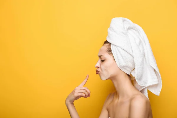 Vista lateral da menina com máscara facial hidratante apontando com o dedo para os lábios no fundo amarelo — Fotografia de Stock