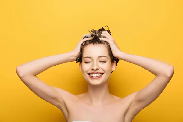 Cheerful girl smiling with closed eyes washing hair on yellow background — Stock Photo