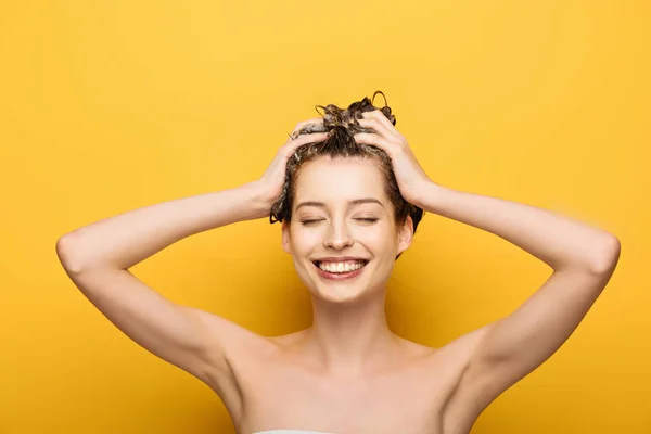 Alegre chica sonriendo con los ojos cerrados lavando el pelo sobre fondo amarillo — Stock Photo