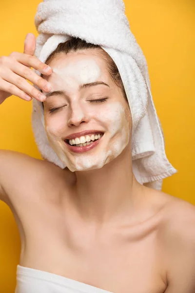 Menina feliz com hidratante facial máscara tocando rosto com olhos fechados no fundo amarelo — Fotografia de Stock