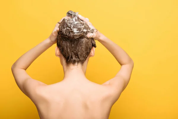 Вид ззаду оголеної жінки, що миє волосся з шампунем на жовтому фоні — стокове фото
