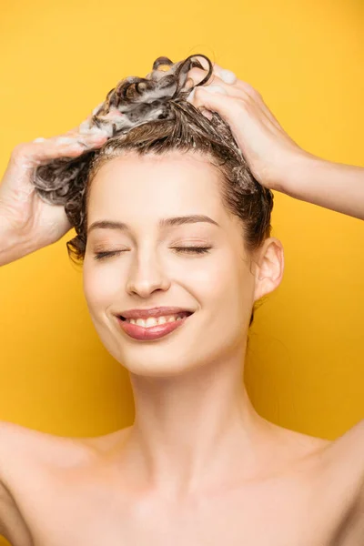 Усміхнена дівчина з закритими очима миє волосся на жовтому фоні — стокове фото