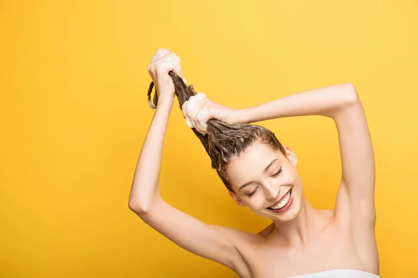 Happy girl smiling with closed eyes while washing long hair on yellow background — Stock Photo