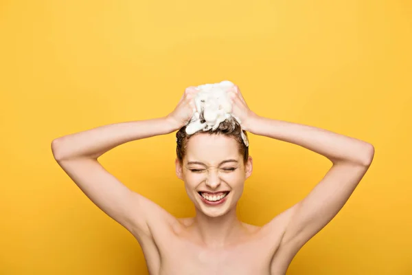 Весела дівчина посміхається із закритими очима під час миття волосся на жовтому фоні — стокове фото