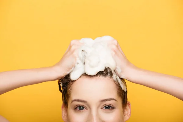Обрізаний вид дівчини миє волосся, дивлячись на камеру ізольовано на жовтому — стокове фото