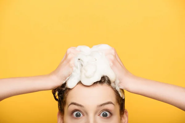 Обрезанный вид взволнованной девушки с широко открытыми глазами, смотрящей в камеру во время мытья волос изолированы на желтый — стоковое фото