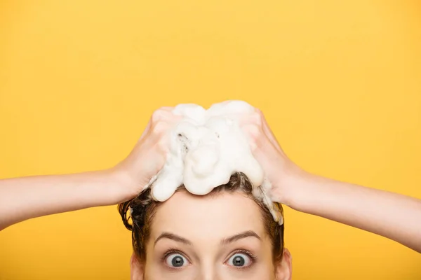 Cropped view of excited girl with wide open eyes looking at camera while washing hair isolated on yellow — Stock Photo