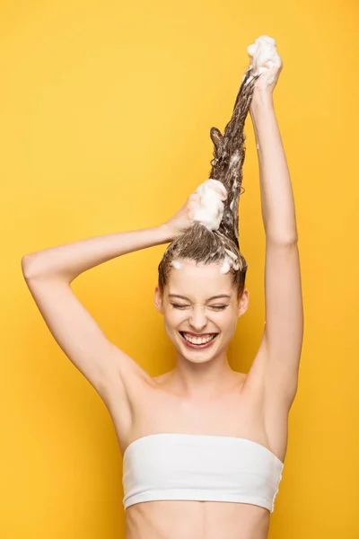 Весела дівчина з закритими очима під час миття довгого волосся на жовтому фоні — Stock Photo