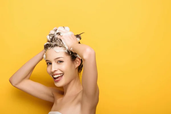 Glückliches Mädchen schaut in die Kamera, während es sich die Haare auf gelbem Hintergrund wäscht — Stockfoto