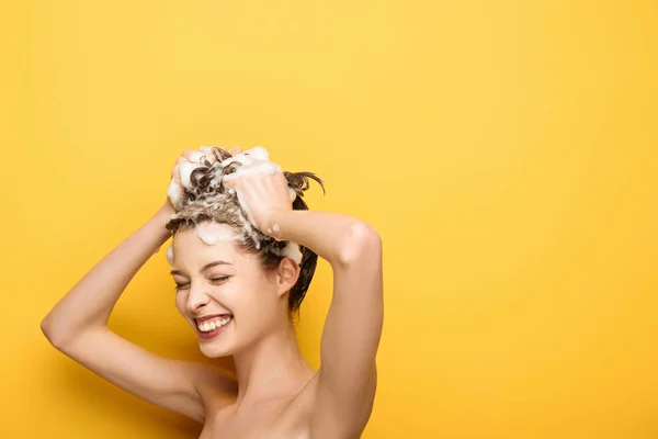 Весела дівчина з закритими очима миє волосся на жовтому фоні — стокове фото