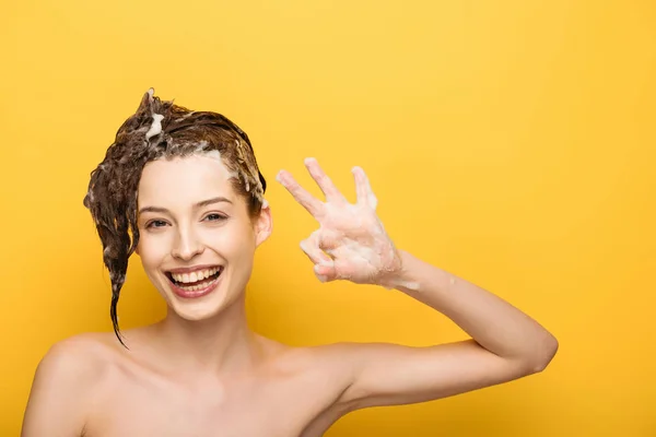 Fille heureuse avec des cheveux savonneux montrant geste correct tout en regardant la caméra sur fond jaune — Photo de stock