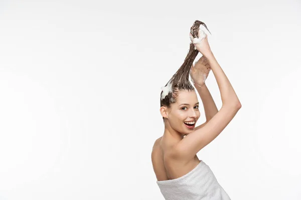 Menina bonita sorrindo para a câmera enquanto lava o cabelo longo isolado no branco — Fotografia de Stock