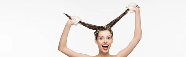 Tiro panorâmico de menina animada se divertindo enquanto lava cabelos longos isolados no branco — Fotografia de Stock
