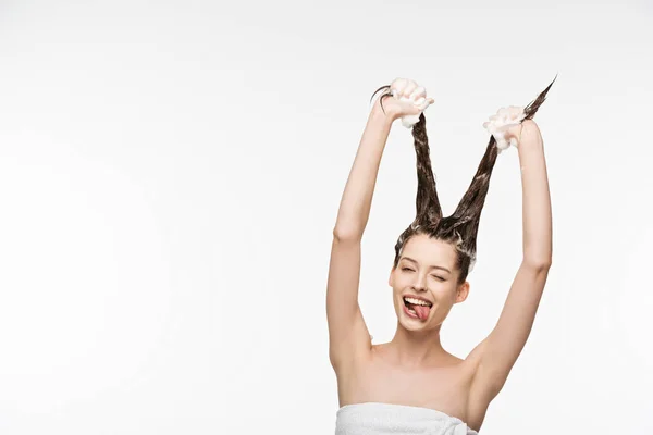 Cheerful girl having fun and sticking out tongue while washing long hair isolated on white — Stock Photo