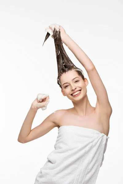 Счастливая девушка смотрит в камеру во время мытья длинные волосы изолированы на белом — стоковое фото